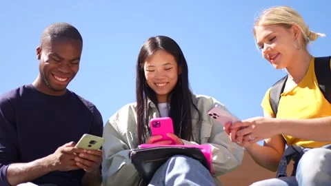 Students using mobile phone sitting on campus bench Stock Footage 299699156