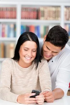 Students using mobile phone together in library Stock Photos