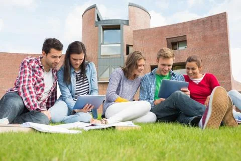 Students using tablet PCs in the lawn against college building Foto stock