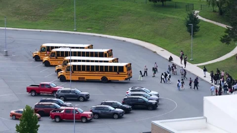 Students walk across busy school parking lot toward row of parked yellow buses Stock Footage 345727711