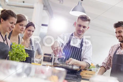 Students watching chef teacher at frying pan in cooking class kitchen Stock Photos