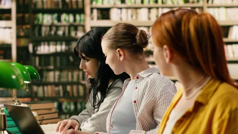 Students working side by side at library table using laptop and open books Stock Footage 336360371