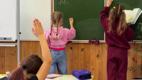 Students writing math equations on a green classroom blackboard while peers.. Stock Footage 339860762