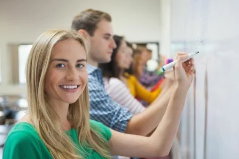 Students writing on the whiteboard together in class with one smiling at camera 스톡 사진