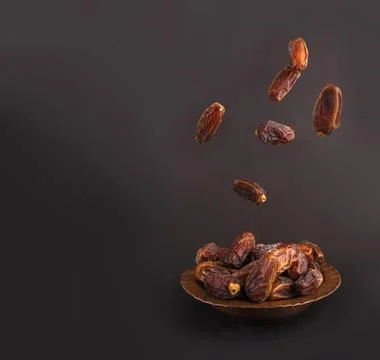 Studio image front eye view of date fruits falling to plate black background. Stock Photos