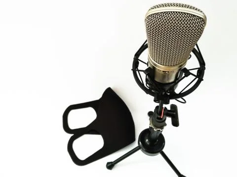 A studio microphone stands on a white background with a black medical mask. Stock Photos