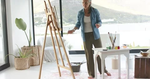 In studio painter is adjusting canvas, dipping brush and applying strokes to Stock Footage 341393492