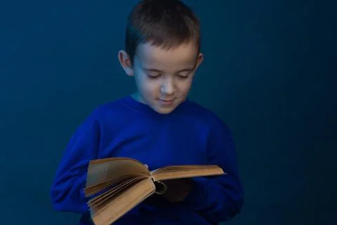 Studio portrait of boy on a blue background in a classic t-shirt. Holding a b 스톡 사진