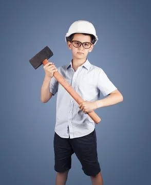 Studio portrait of a boy worker in a hard hat with a hammeron a blue background Stock Photos