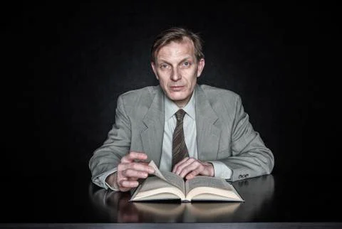 Studio portrait of caucasian man actor seated reading from an open book. Stock Photos