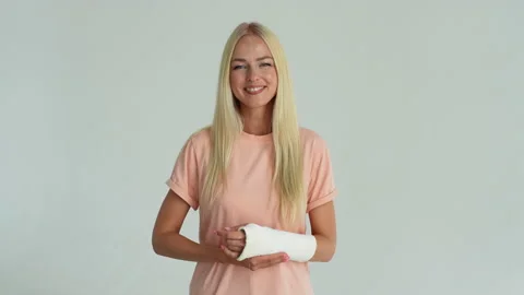 Studio portrait of cheerful blonde young woman with broken arm wrapped in white Stock Footage 220272230