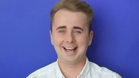 Studio portrait of confident smiling young man laughing against blue background Stock Footage 219092790