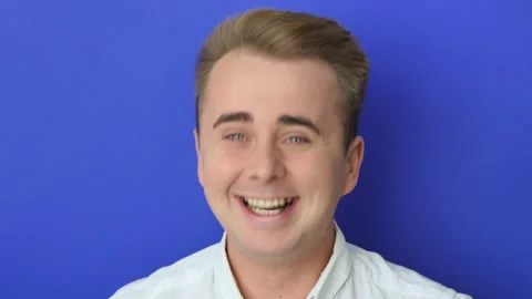 Studio portrait of confident smiling young man laughing against blue background Stock Footage 219540865