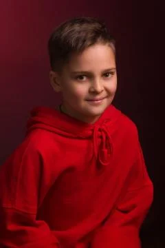 Studio portrait of a dark-haired boy, on a maroon background, in a red hoodie Stock Photos