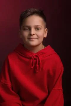 Studio portrait of a dark-haired boy, on a maroon background, in a red hoodie 스톡 사진