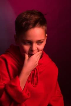 Studio portrait of a dark-haired boy, on a maroon background, in a red hoodie Stock Photos