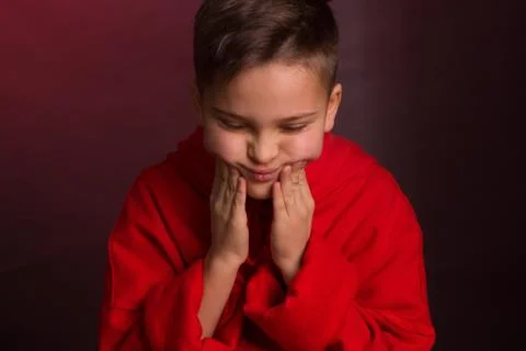 Studio portrait of a dark-haired boy, on a maroon background, in a red hoodie Stock Photos