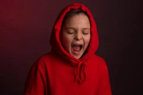 Studio portrait of a dark-haired boy, on a maroon background, in a red hoodie Stock Photos
