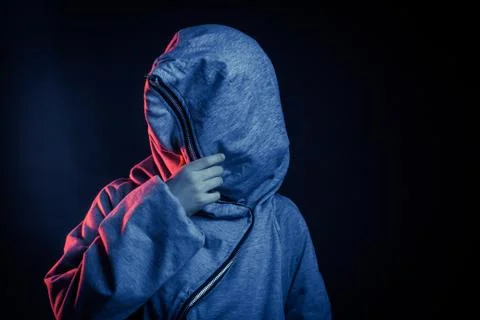 Studio portrait of a dark-haired boy, on a dark background, in a hoodie jacke Stock Photos