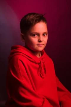 Studio portrait of a dark-haired boy, on a maroon background, in a red hoodie Stock Photos