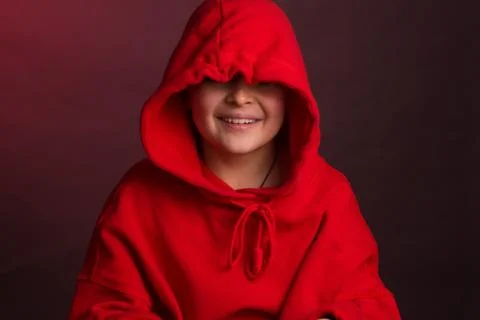 Studio portrait of a dark-haired boy, on a maroon background, in a red hoodie Stock Photos