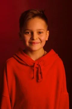 Studio portrait of a dark-haired boy, on a maroon background, in a red hoodie Stock Photos