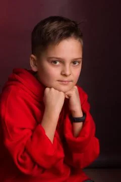 Studio portrait of a dark-haired boy, on a maroon background, in a red hoodie Stock Photos