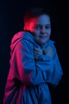 Studio portrait of a dark-haired boy, on a dark background, in a hoodie jacke Stock Photos