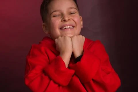 Studio portrait of a dark-haired boy, on a maroon background, in a red hoodie Stock-Fotos