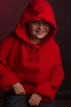 Studio portrait of a dark-haired boy, on a maroon background, in a red hoodie Stock Photos
