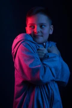 Studio portrait of a dark-haired boy, on a dark background, in a hoodie jacke Stock Photos