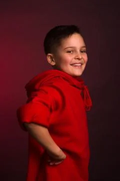 Studio portrait of a dark-haired boy, on a maroon background, in a red hoodie Stock Photos