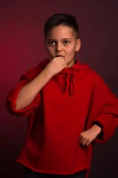 Studio portrait of a dark-haired boy, on a maroon background, in a red hoodie Stock Photos