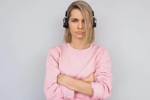 Studio portrait of grumpy young female wearing pink sweater, with headphones  Stock Photos