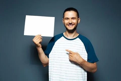Studio portrait of guy point finger on white empty paper board. Blue backgrou Stock Photos