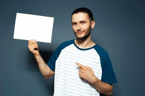 Studio portrait of guy point finger on white empty paper board. Blue backgrou Stock Photos