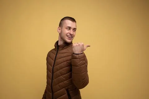 Studio portrait. Young 20s man in brown jacket, on yellow background, smiling Stock Photos