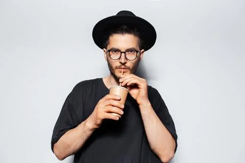 Studio portrait of young guy drinking cold tea with straw from paper cup. Stock Photos