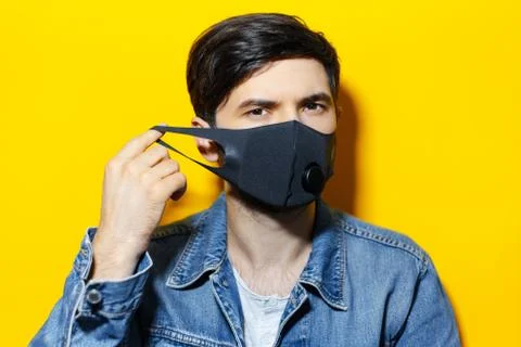 Studio portrait of young guy, putting on black respiratory face mask. Stock Photos