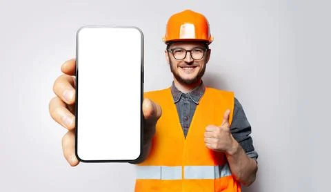 Studio portrait of young smiling construction worker, holding big smartphone  Stock Photos
