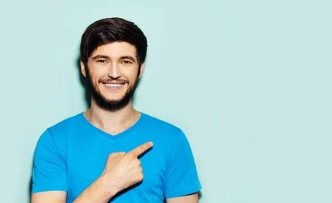 Studio portrait of young smiling guy in blue shirt, pointing with finger. Stock Photos