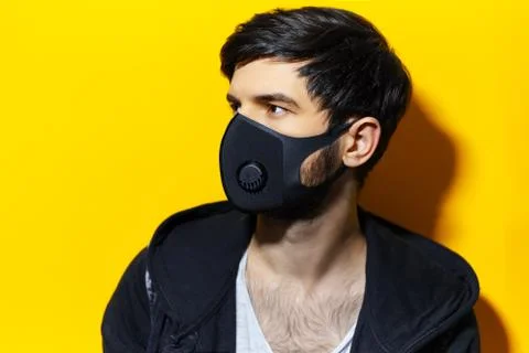 Studio profile portrait of young guy wearing black respiratory face mask. Stock Photos