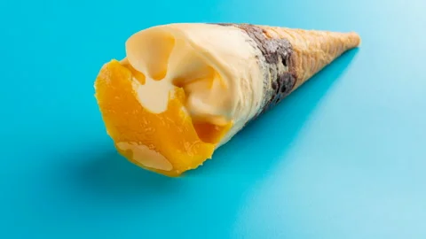 Studio shoot mini mango or orange flavor ice cream cone melting on blue Stock Footage 92282221