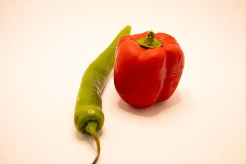 A studio shot featuring a long green chili pepper placed beside a ripe red be Stock Photos