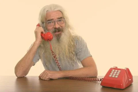 Studio shot of happy senior bearded man smiling while talking on old telephone Stock Photos