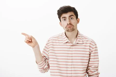 Studio shot of miserable upset nerdy guy with beard and moustache, pointing left Photos