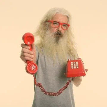 Studio shot of senior bearded man giving old telephone Stock Photos