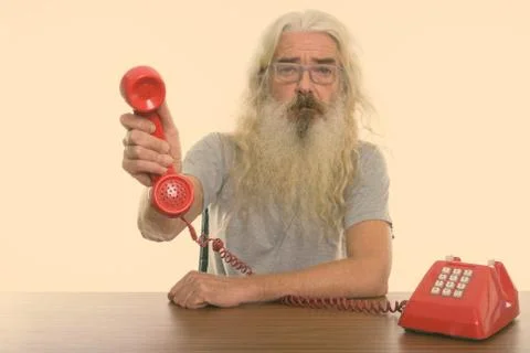 Studio shot of senior bearded man giving old telephone on wooden table Stock Photos