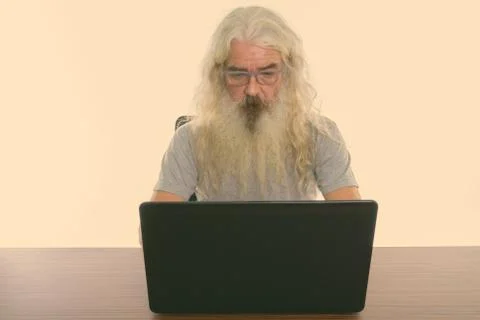 Studio shot of senior bearded man using laptop on wooden table Stock Photos