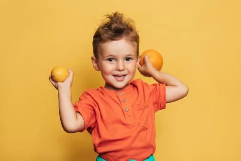 Studio shot of a smiling boy holding a fresh lemon and orange on a yellow Stock Photos